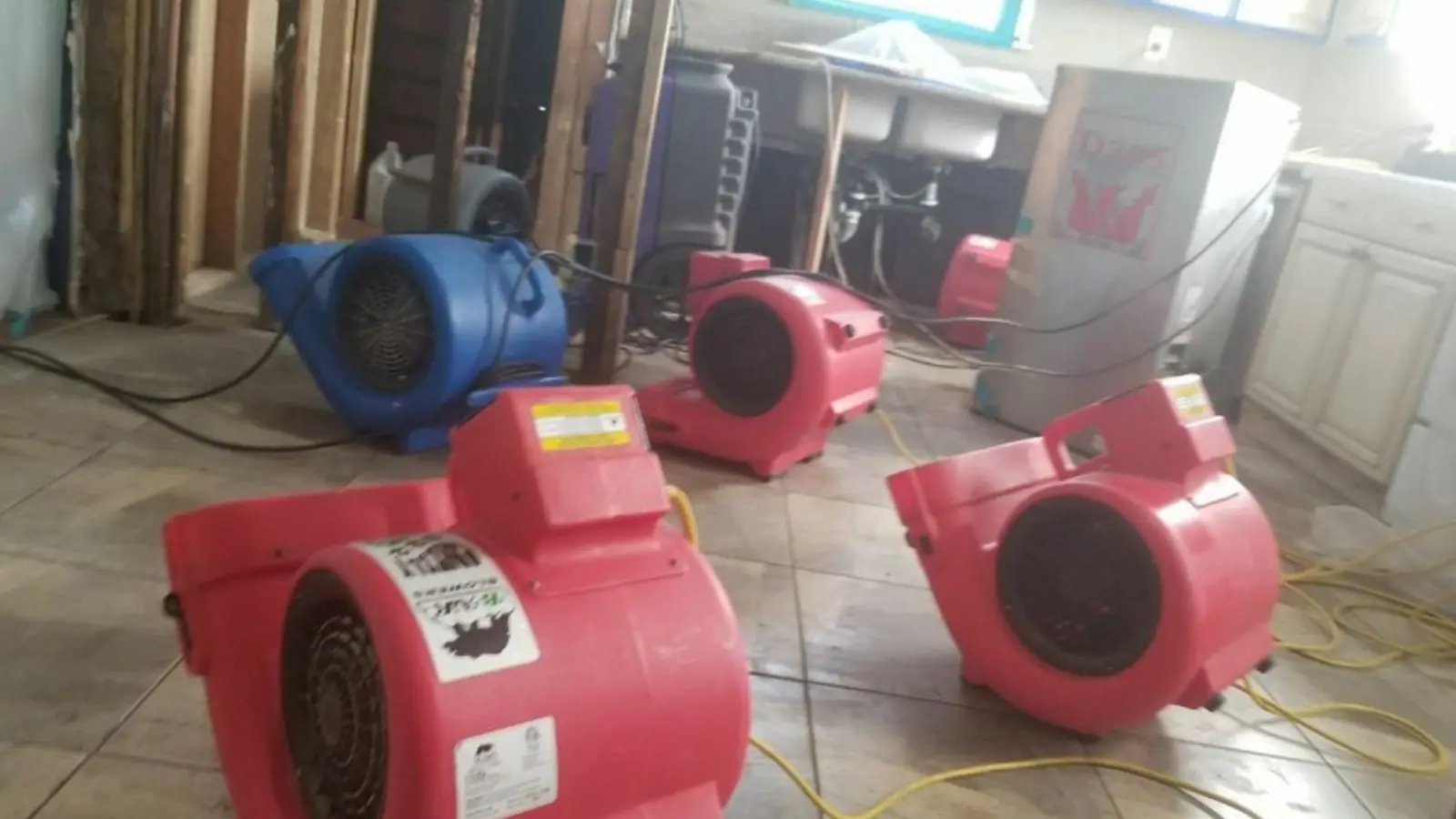 Red air movers drying a tiled room beside exposed wall framing