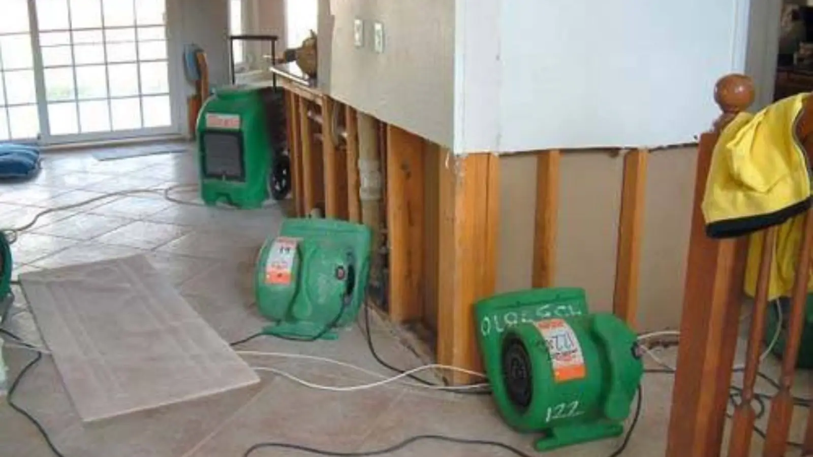 Air movers running in a room where lower wall sections have been cut out to dry the framing